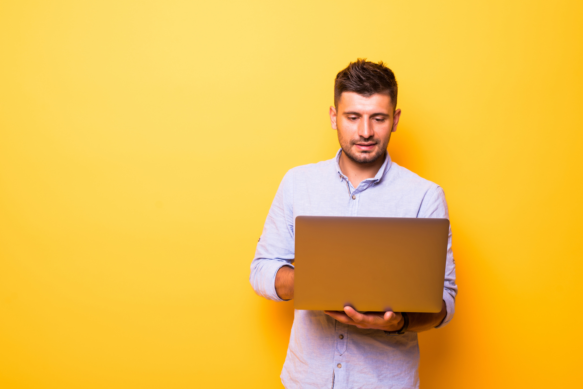 Young handsome man with laptop on yellow background